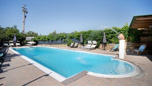Une piscine rectangulaire, bordée d’une terrasse carrelée, entourée de chaises longues et de parasols.