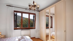 Une chambre avec une grande fenêtre, un lit recouvert d’une literie à motifs floraux, un radiateur et une armoire.