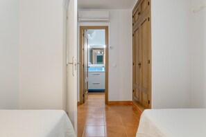 A narrow hallway with two beds on either side, leading to a bathroom with a mirror and a sink.