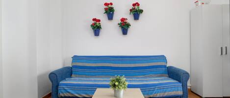 A room with a blue sofa, a small table with a plant, and four potted plants on the wall.