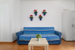 Une pièce avec un canapé bleu, une petite table sur laquelle est posée une plante, et quatre plantes en pot accrochées au mur.