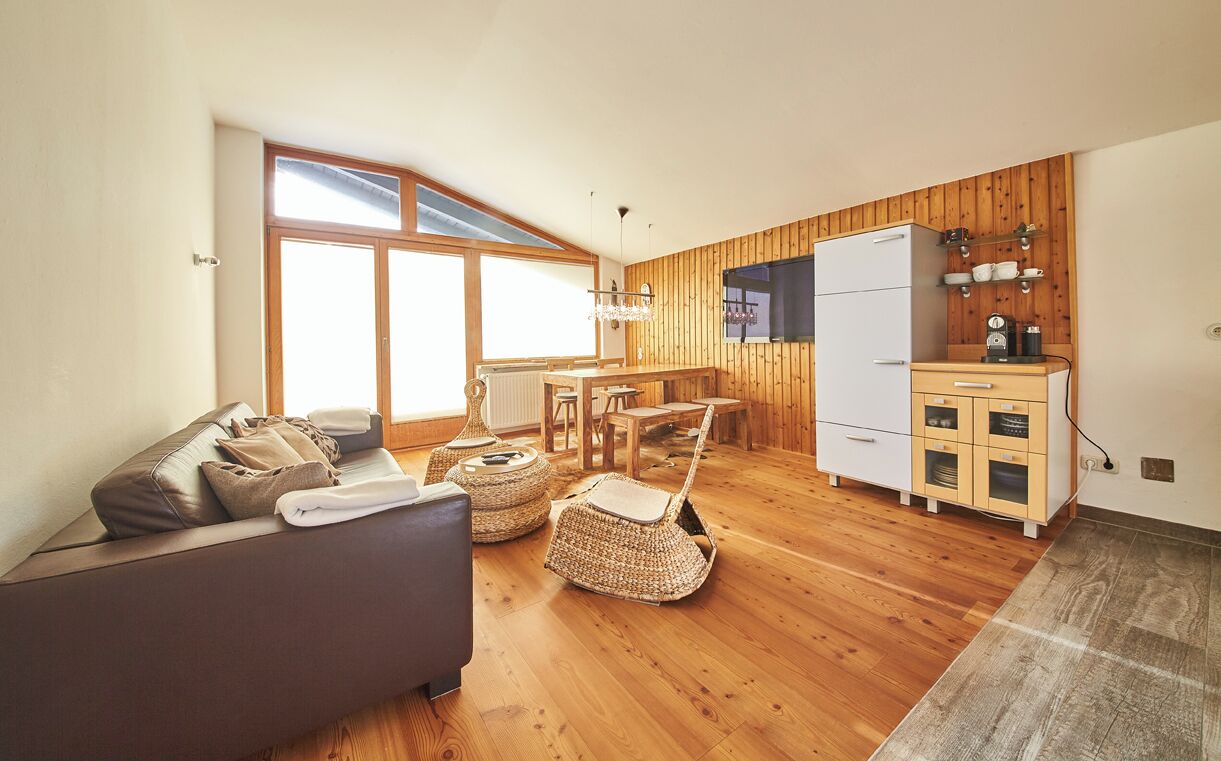 A cozy living room with a sofa, chairs, a dining table, and a kitchen area with a refrigerator and cabinets.