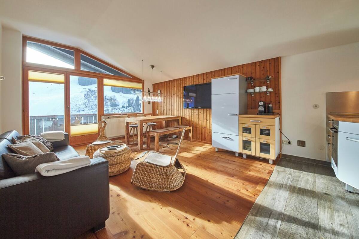 Un salon moderne comprenant un canapé, des fauteuils en osier, une table à manger et un coin cuisine avec des meubles en bois et un réfrigérateur.