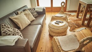 A living room with a brown leather sofa, two woven side tables, and a wooden dining table. - SunnySide Appartements (Hinterglemm)