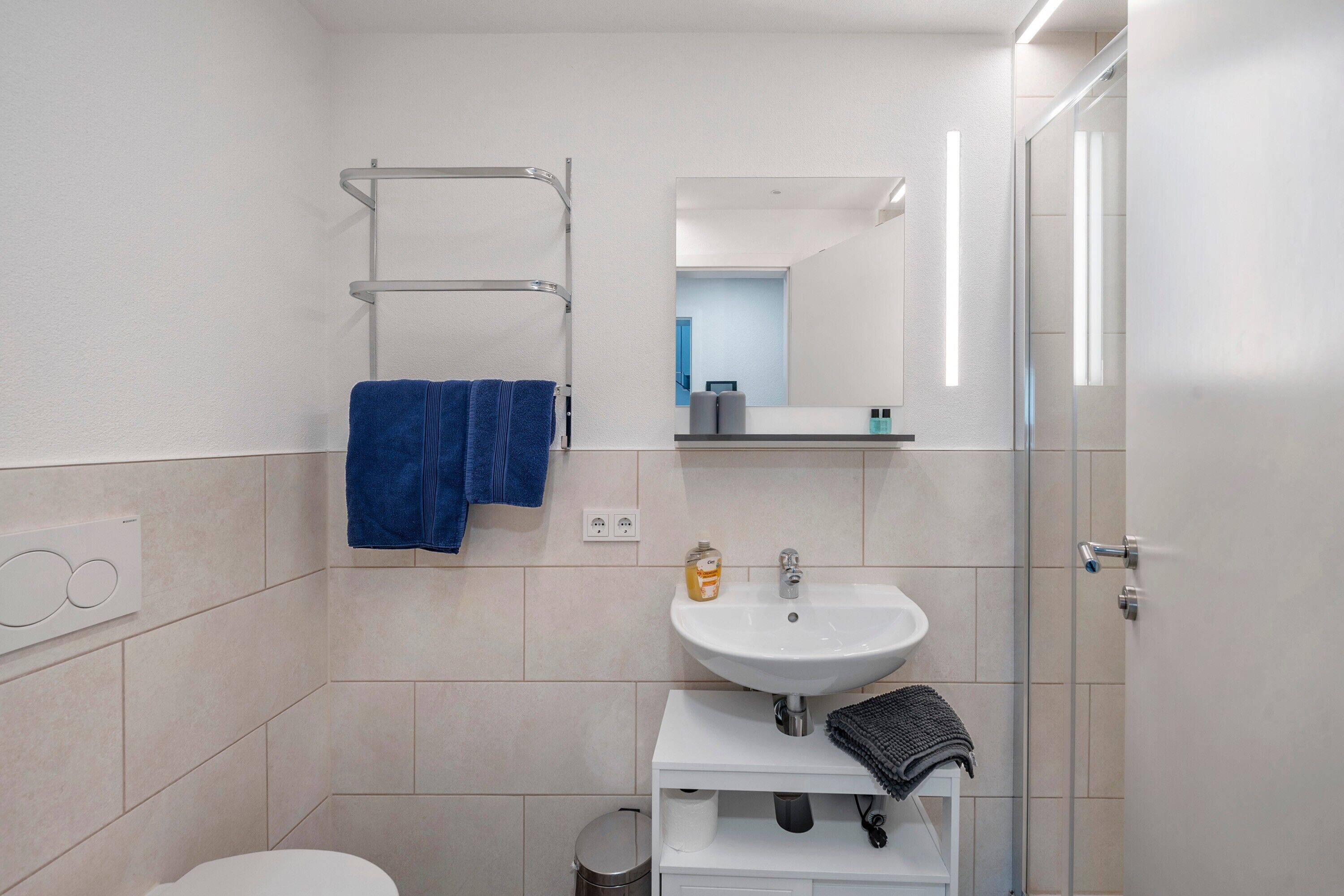 Une salle de bain moderne avec un lavabo blanc, un miroir et un porte-serviettes.