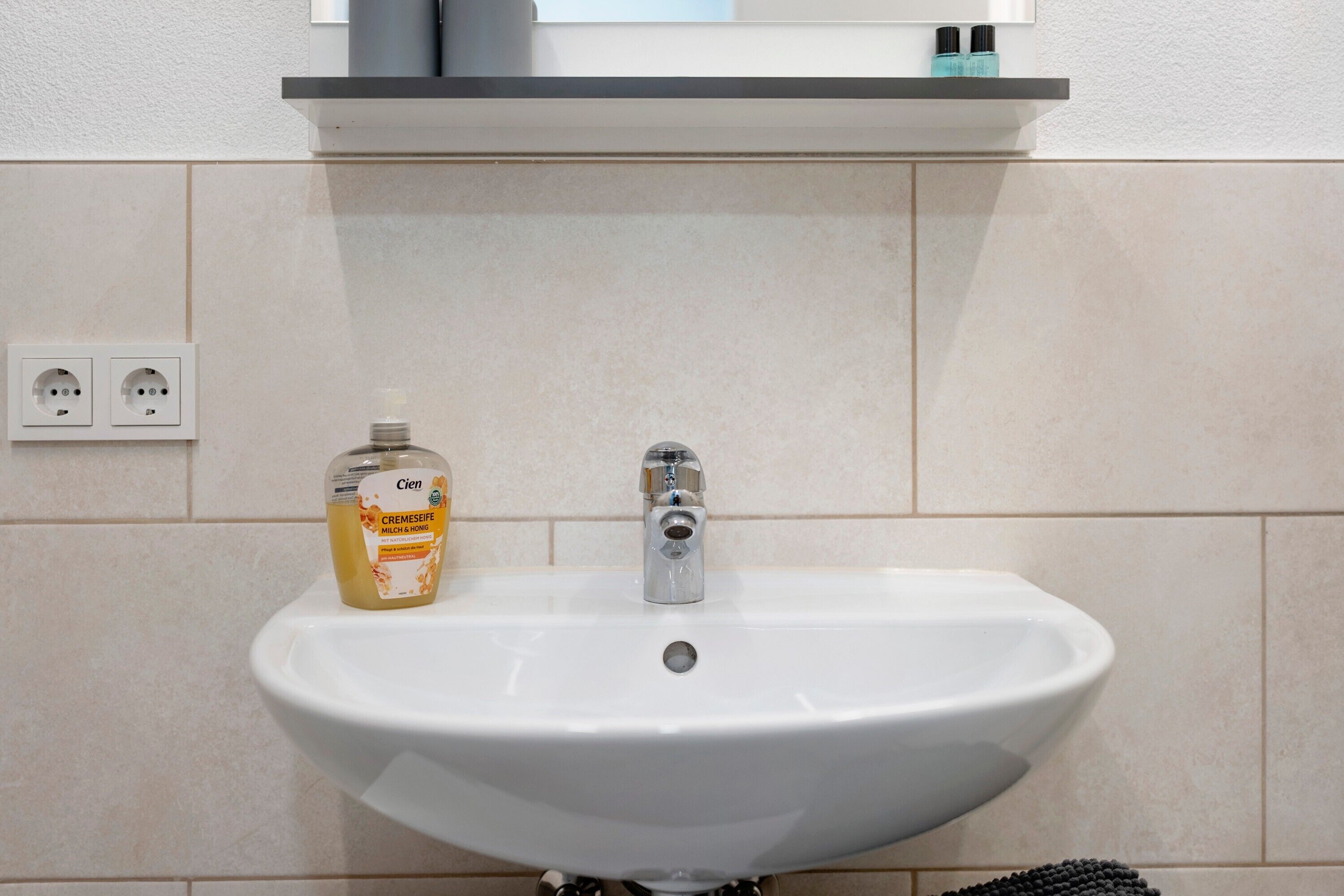 A white bathroom sink with a single faucet, a soap dispenser, and a mirror above it.