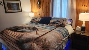 Una cama con una manta texturizada, un reloj en la pared y una mesita de noche con una lámpara.
