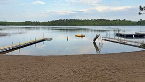 Un lago tranquilo con un muelle de madera que se adentra en el agua, rodeado por una playa de arena.