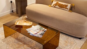 A living room with a sofa, a glass coffee table with magazines, and a small wooden side table.