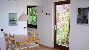 A dining area with a wooden table and chairs, a window with a view of greenery, a door with a key, and a wall-mounted lamp. - Studio 'Unterschütz' with Mountain View, Private Terrace and Wi-Fi (Ettenheim)