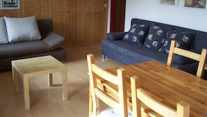 A room with a wooden floor, a grey sofa, a blue sofa with patterned cushions, a wooden table, and a small wooden stool. - Studio 'Unterschütz' with Mountain View, Private Terrace and Wi-Fi (Ettenheim)