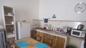 A compact kitchen with a wooden table, chairs, a microwave, and a sink. - Le lierre Seasonal rental, 10mn from la de ste croix, close to all shops (Aiguines)
