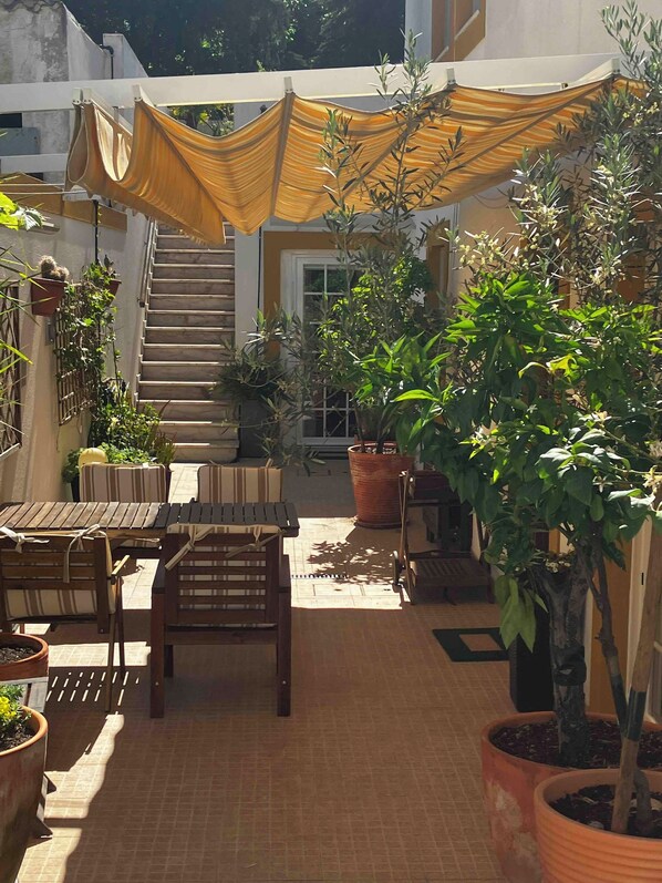 An outdoor patio area with a wooden table and chairs, potted plants, and a staircase leading to an upper level.