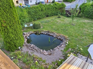 Un bassin circulaire bordé de pierres, entouré d’une pelouse bien entretenue et d’un grand arbre à feuilles persistantes.