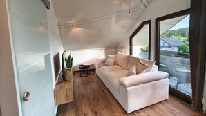 A modern loft bedroom with a large window, a white sofa, a small round table, and a wooden floor. - Holiday Apartment 'Andreas' with Mountain View and Wi-Fi (Sankt Blasien)