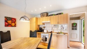 A modern kitchen with wooden cabinets, a dining table with chairs, and a hanging pendant light. - Holiday Home 'Bungalow 73' with Private Terrace and Private Garden (Zadelsdorf)