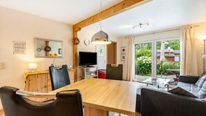 A dining area with a wooden table, black chairs, a TV, and a view of the outdoors. - Holiday Home 'Bungalow 73' with Private Terrace and Private Garden (Zadelsdorf)
