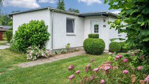 A single-story building with a white exterior, a door with a wreath, and a small window. - Holiday Home 'Bungalow 73' with Private Terrace and Private Garden (Zadelsdorf)