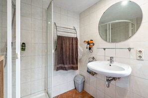 A bathroom with a glass shower enclosure, a white sink, a mirror, and a towel rack.