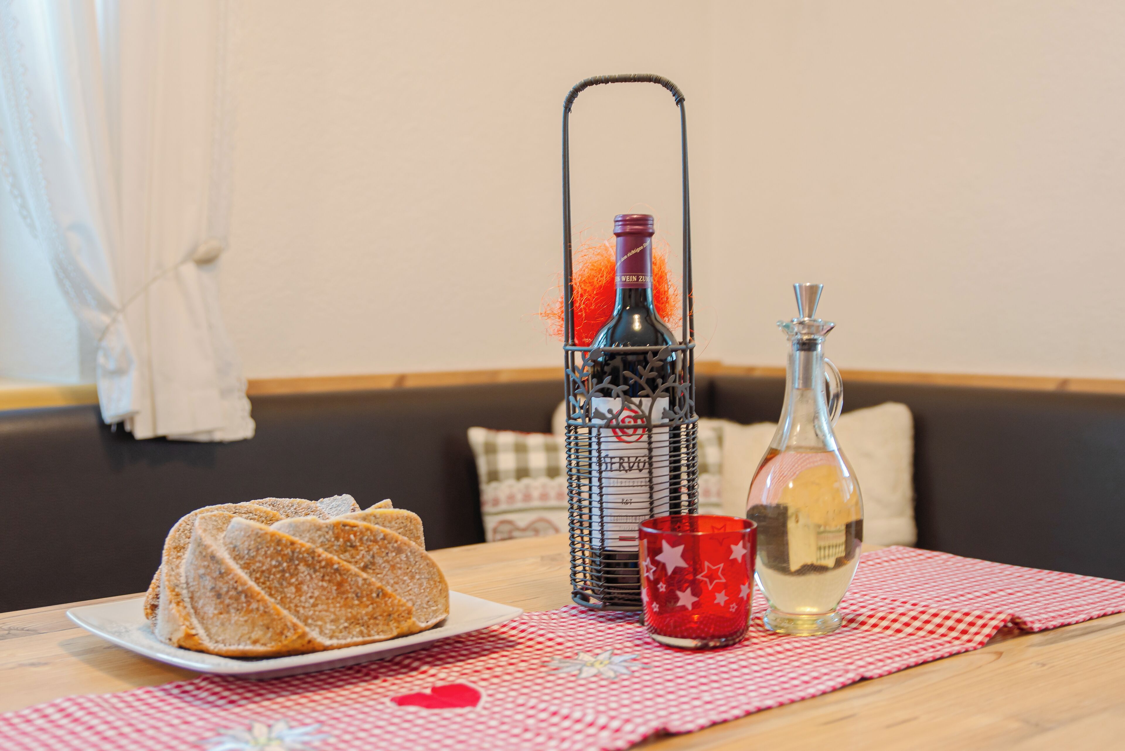 A table with a checkered tablecloth, a plate of sliced bread, a candle holder, and a bottle of water.