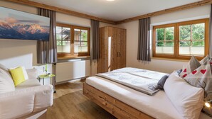 Une chambre à coucher avec un lit en bois, un canapé, une télévision et de grandes fenêtres avec des rideaux.