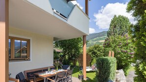 Une terrasse extérieure avec une table et des chaises, un banc en bois et une vue sur un jardin et des collines.