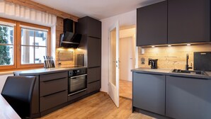 Une cuisine moderne avec des meubles de couleur sombre, un four encastré et une fenêtre équipée de stores.