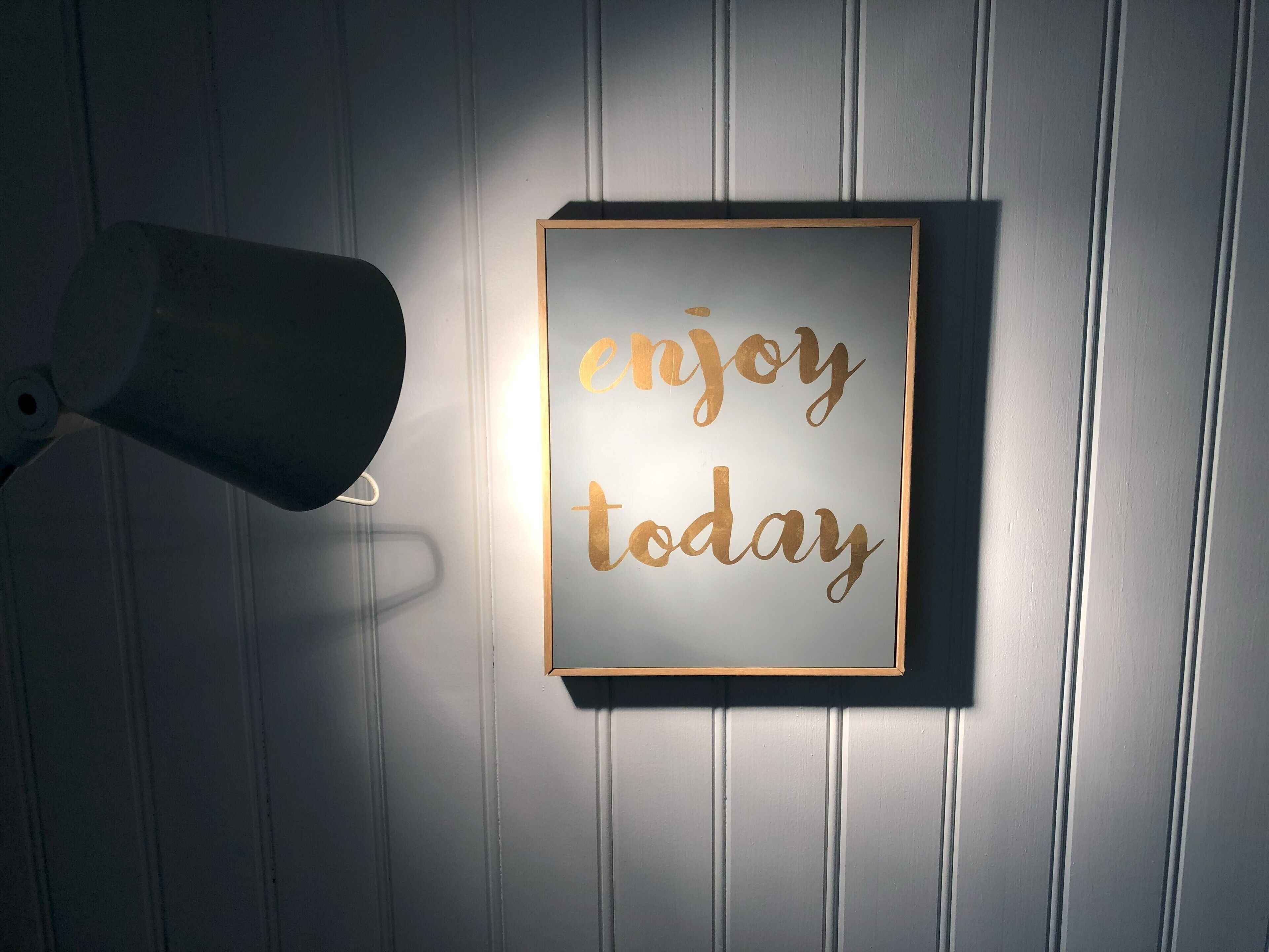 A wall-mounted sign with the text "enjoy today" in a decorative font, framed in a simple wooden border.