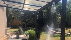 Een overdekt terras met een tafel, stoelen, een hanglamp en een waterslang.