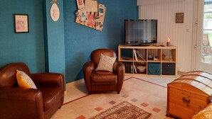Een woonkamer met een blauwe wand, een televisie, een houten kast en twee leren banken.