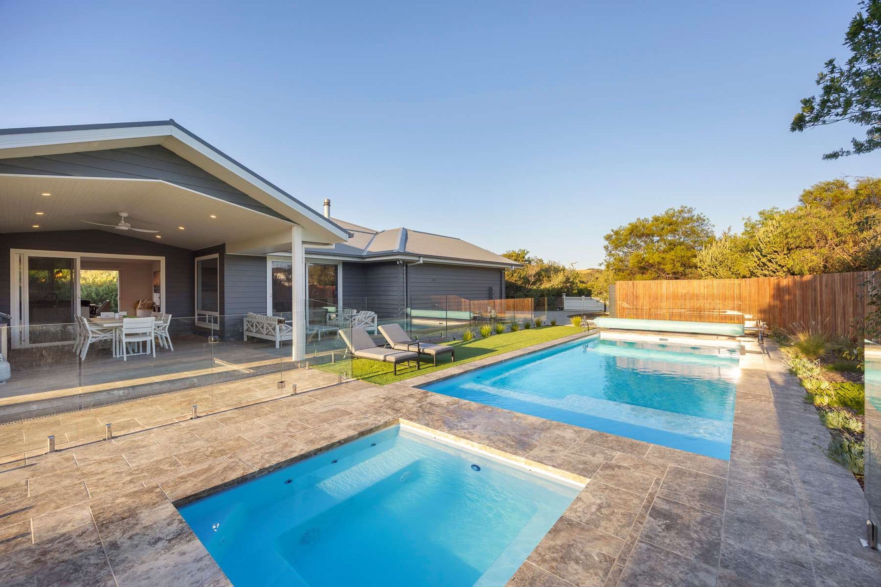 A modern house with a swimming pool, patio with outdoor furniture, and a covered area with a ceiling fan.