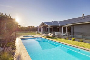 Una casa moderna con piscina, terraza cubierta y césped cuidado.