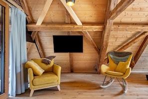 A wooden interior with a sofa and rocking chair, wooden beams, and a TV mounted on the wall.