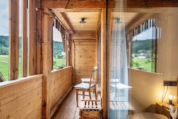 A wooden cabin with a balcony, a chair, and a table.