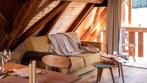 Une chambre mansardée avec un plafond en bois, un canapé, une petite table avec une bougie et une fenêtre donnant sur un beau paysage.