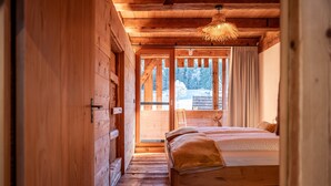 Une chambre à coucher dans une cabane en bois, avec un lit, un luminaire suspendu et une vue sur un paysage enneigé, visible à travers une porte.