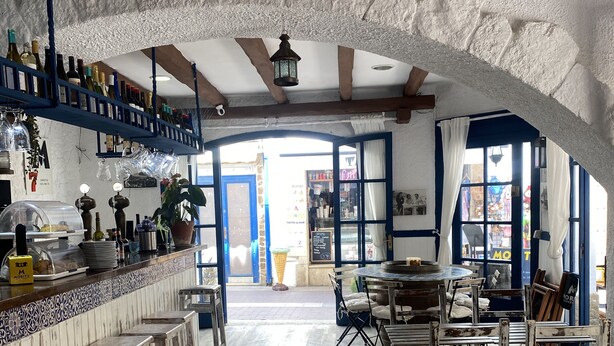 A rustic interior with exposed wooden beams, a bar area with bottles, and a view to the outside. - Hotel & Restaurante Bergantí (Tossa de Mar)