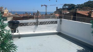 A rooftop terrace with a barbecue grill, string lights, and a view of the sea and buildings. - Hotel & Restaurante Bergantí (Tossa de Mar)