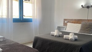 A hotel room with two beds, a wooden headboard, a bedside table, and a window with curtains. - Hotel & Restaurante Bergantí (Tossa de Mar)