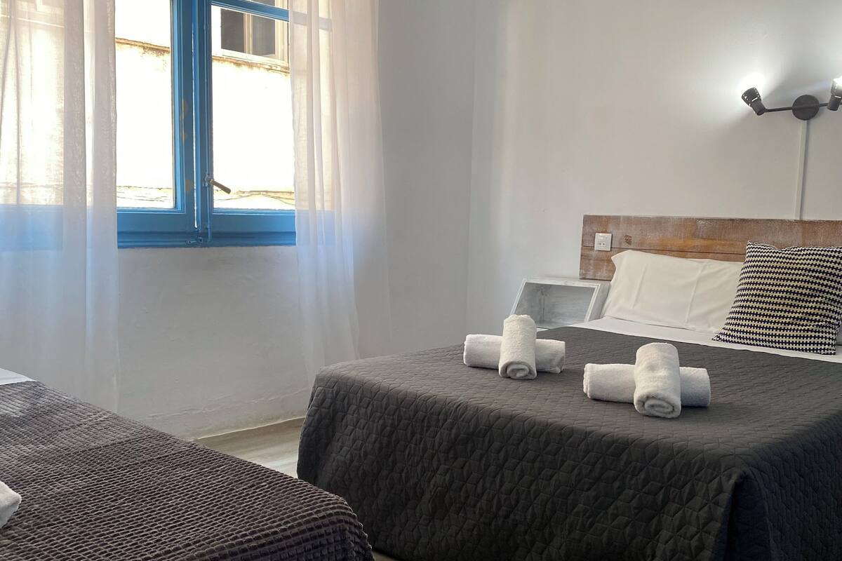 A hotel room with two beds, a wooden headboard, a bedside table, and a window with curtains.