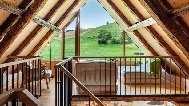Habitación de ático con techos altos y un ventanal con vistas a un paisaje cubierto de hierba.