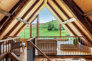 Habitación de ático con techos altos y un ventanal con vistas a un paisaje cubierto de hierba.