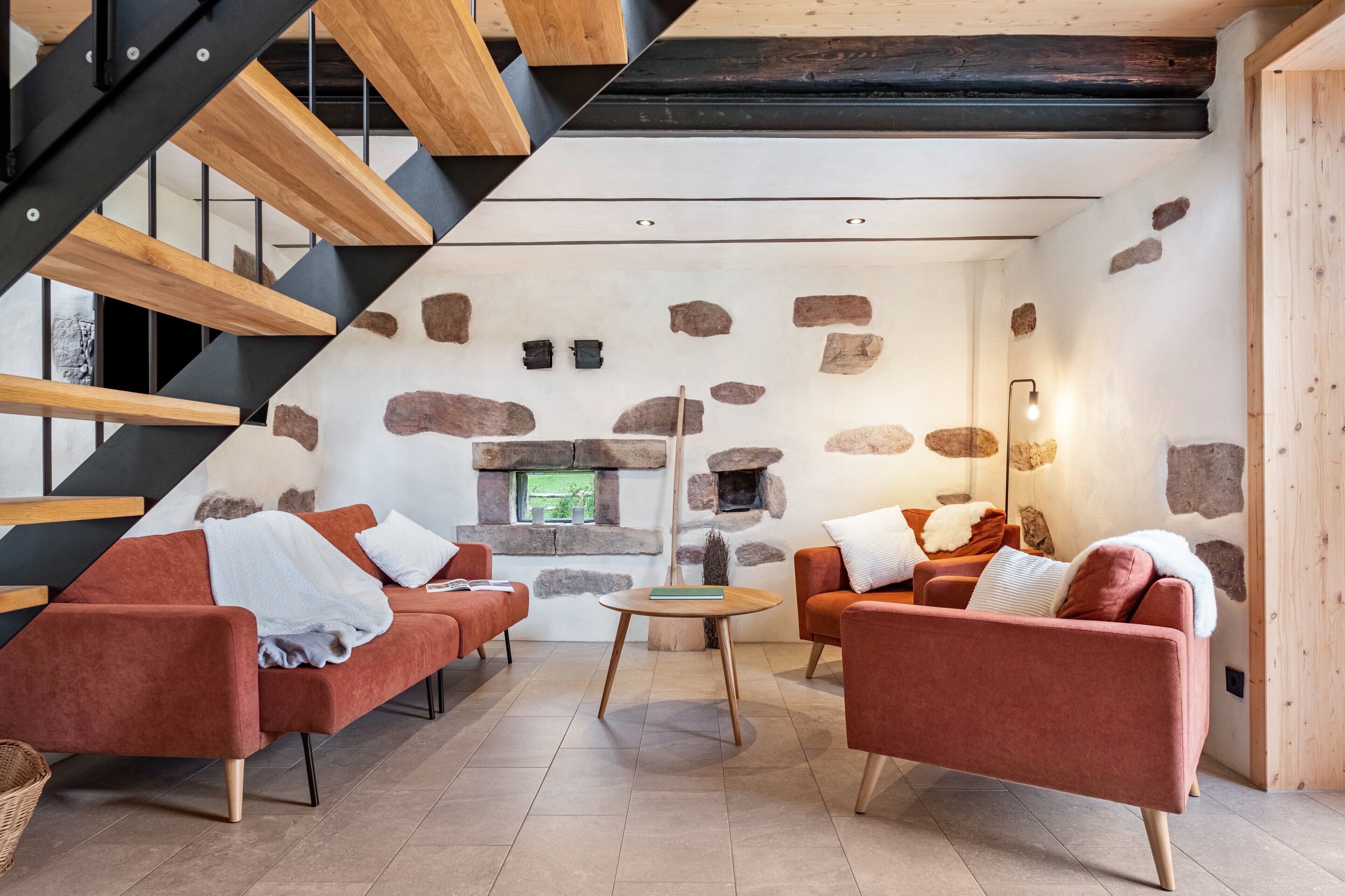 Ein modernes Wohnzimmer mit Steinwand, roten Sofas, einer Holztreppe und einem kleinen Kamin.