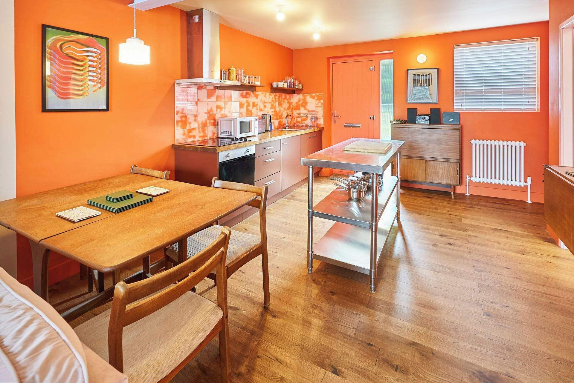 A compact kitchen with a microwave, stove, and cabinets, a dining table with chairs, and a radiator.