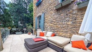 A stone building with a stone wall, a balcony with a railing, and outdoor furniture including a sofa and a bench. - Maison d'Or (Saint-Cyr-au-Mont-d'Or)