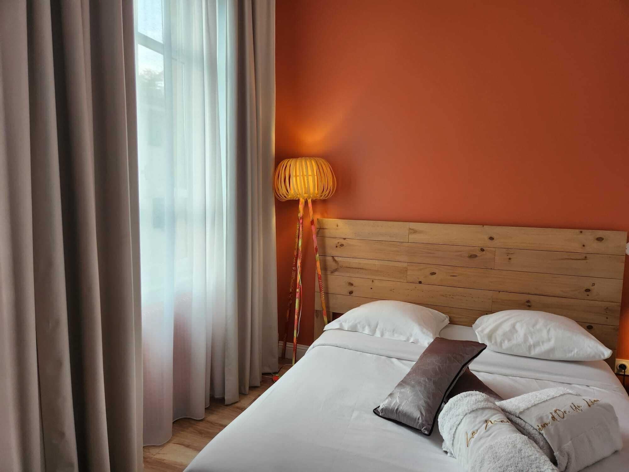 A hotel room with a wooden headboard, a bed with white linens, a bedside lamp, and a window with curtains.