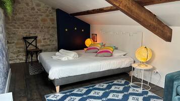 Un dormitorio con pared de piedra, cama con ropa de cama blanca, almohadas coloridas, una lámpara de globo y una alfombra estampada.