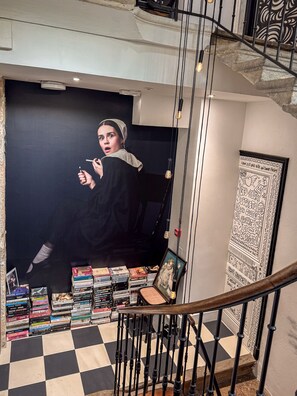 A staircase with a checkered floor, a wall with a framed picture, and a collection of books and DVDs on the floor.