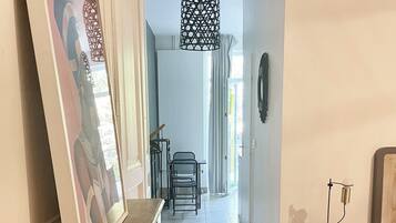 A hallway with patterned floor tiles, a wooden bench, a framed picture on the wall, a hanging light fixture, and a small table with a lamp.