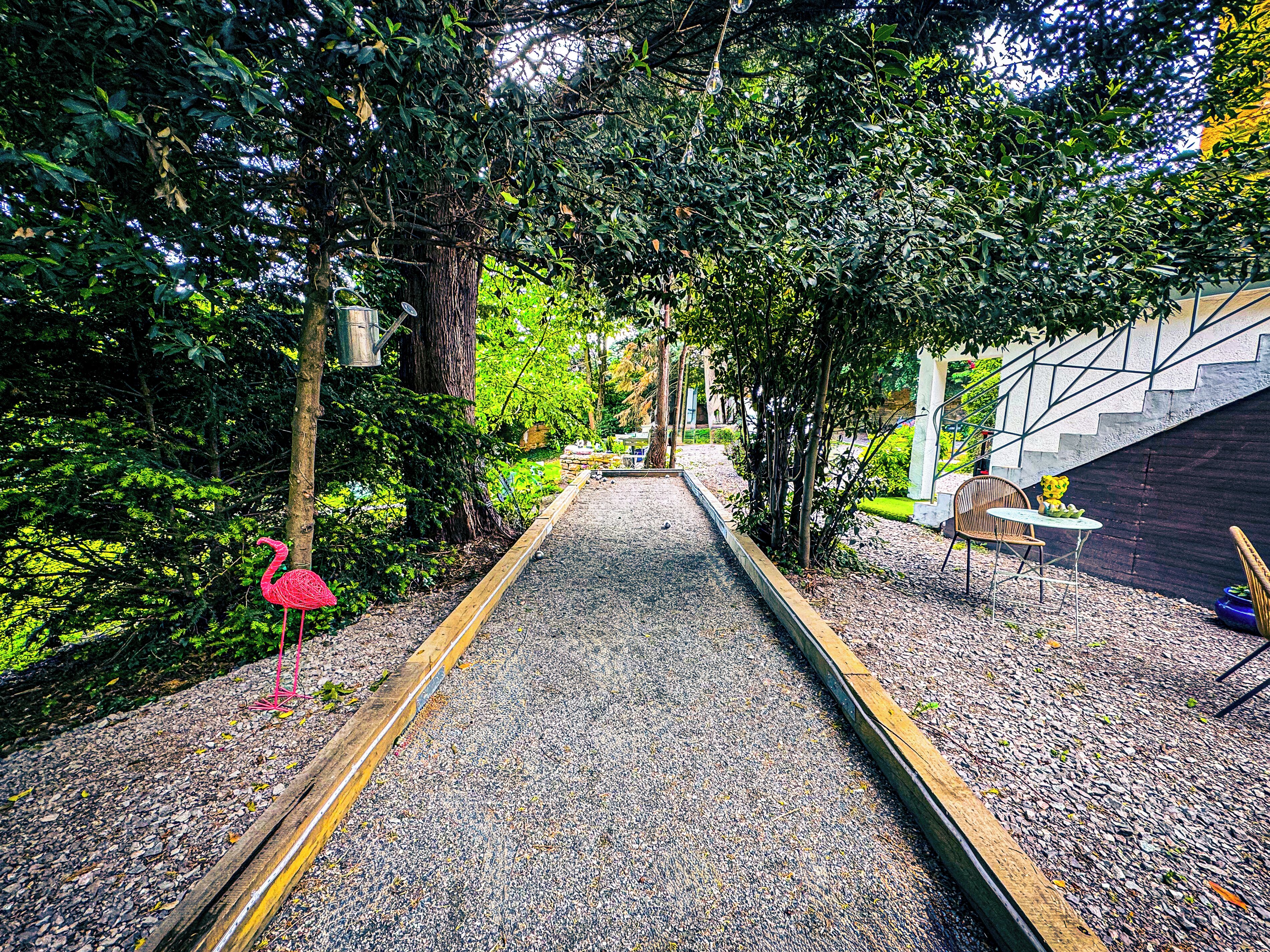 A pathway with a wooden border, surrounded by greenery and a pink flamingo statue.